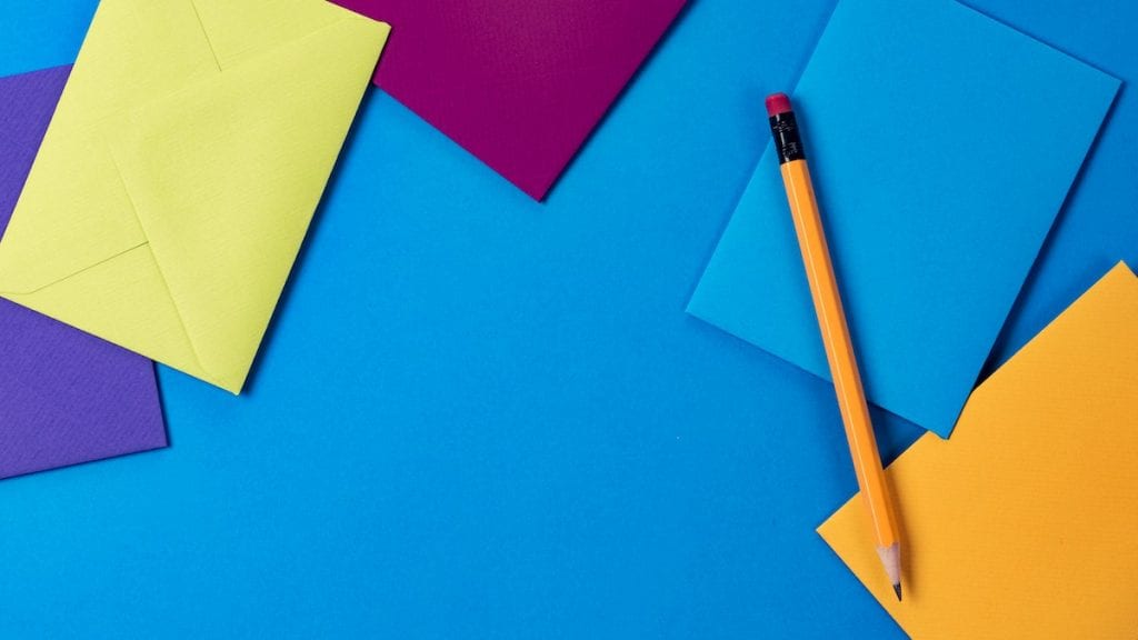 Blue, yellow, orange, and purple envelopes and a pencil sitting on a blue background