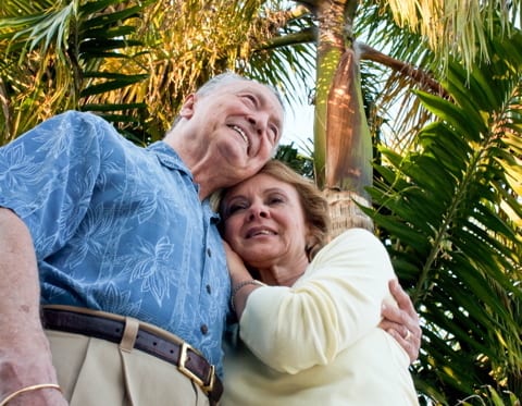 A senior man and woman smile and hug under palm trees | Credit: ARARF