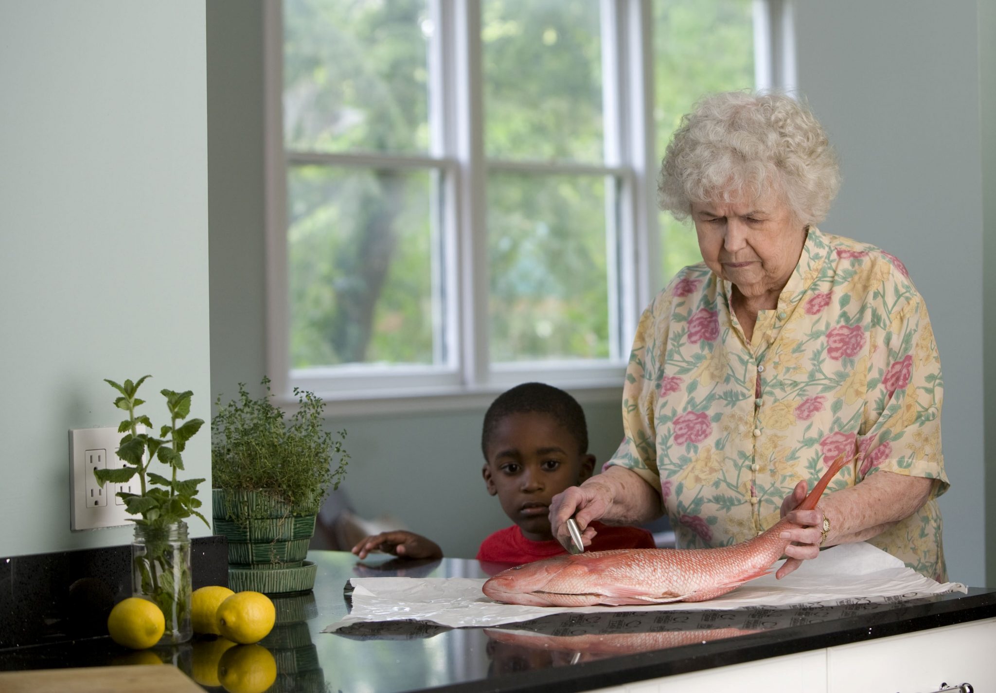An older woman stands at a kitchen table with her grandson